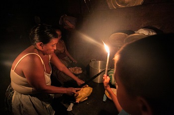 Woman in Pie del Cerro prepares meal by candlelight.