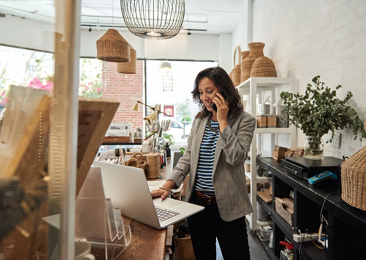 Woman talks on her cellphone while using her laptop while running a small business.