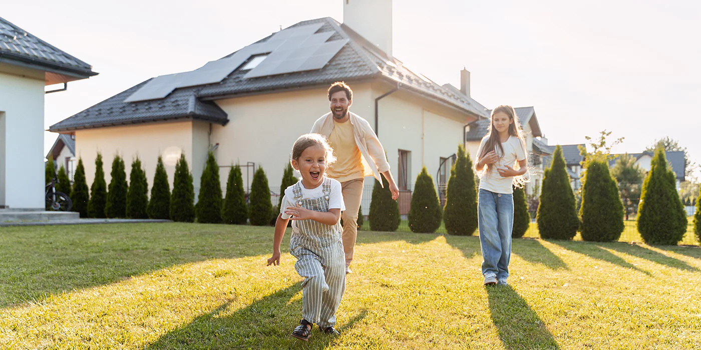 Family runs together in a backyard, home with solar panels in background.