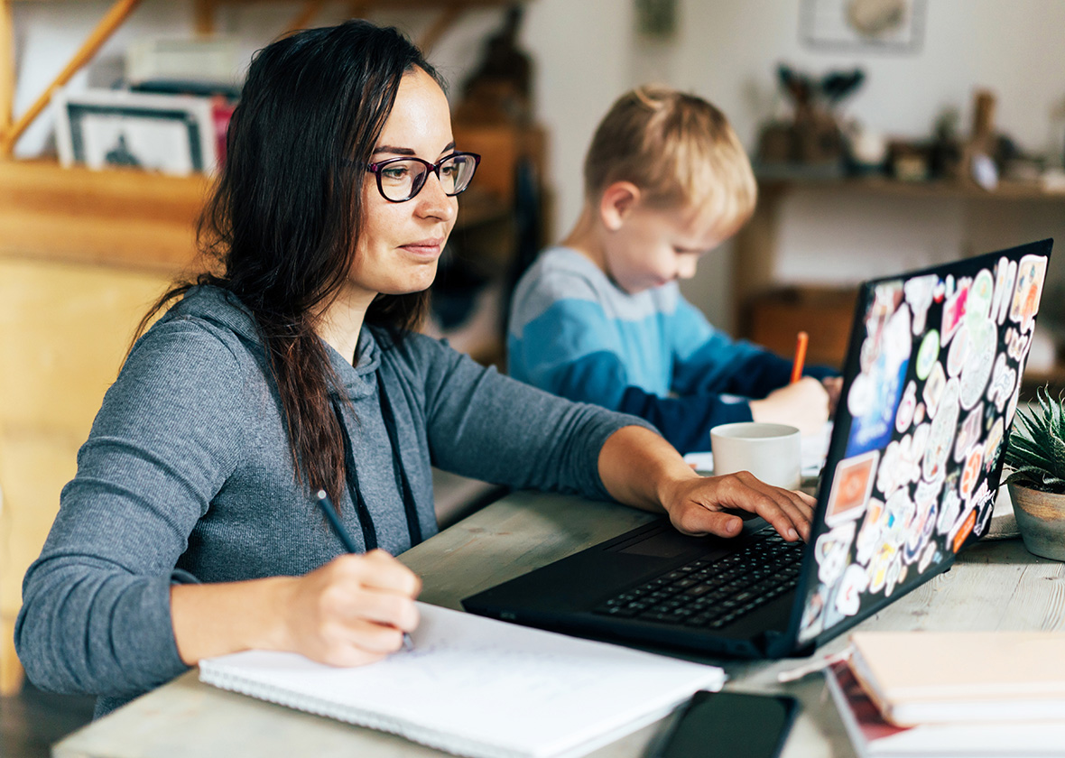 Mom working on school work on her laptop while her son works next to her.
