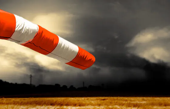 Orange and white windsock blowing strongly against dark storm clouds.