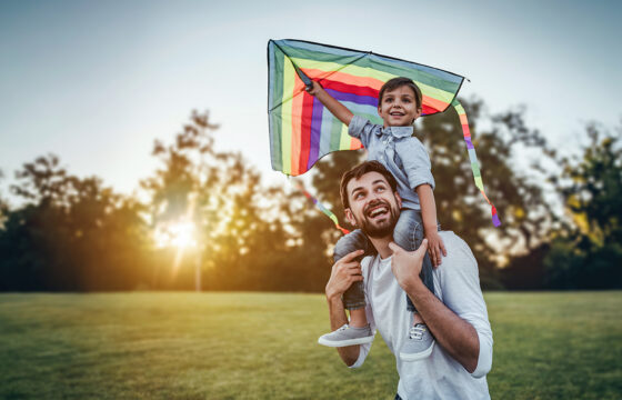 Man holding his child on his shoulders while the child holds a flying kite.