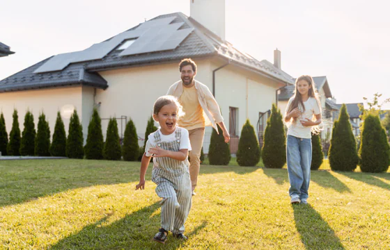 Family runs together in a backyard, home with solar panels in background.