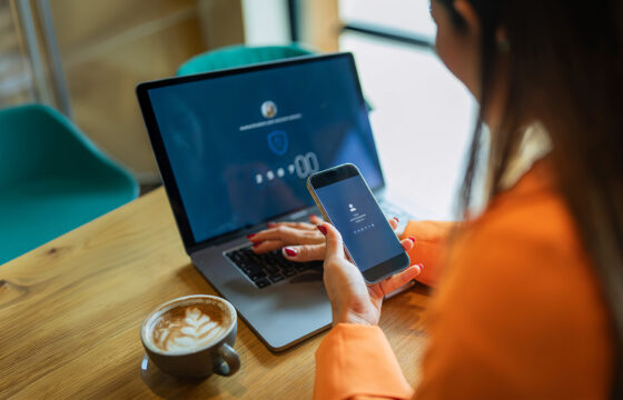 Woman at a coffee shop, entering a 2fa code from her phone onto her laptop.